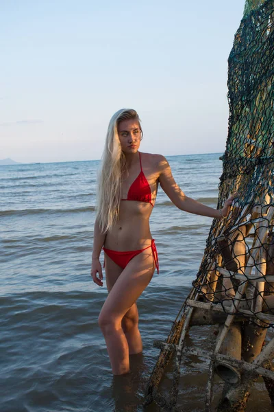 Blonde en maillot de bain rouge dans la mer dans une cage avec une grille — Photo