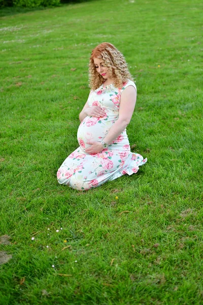 Dziewczyna w ciąży na trawie w parkbushes bzu — Zdjęcie stockowe