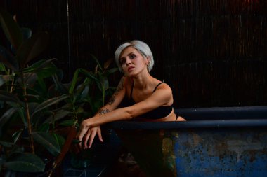 beautiful short-haired girl with tattoo posing in bath. romance.