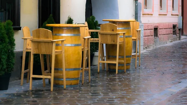 Lege houten stoelen en tafels vaten op straat op regenachtige dag — Stockfoto