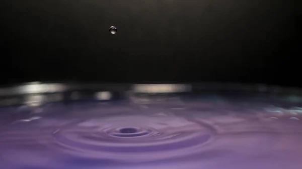Salpicadura de agua en el fondo colorido con una gota de agua volando —  Fotos de Stock