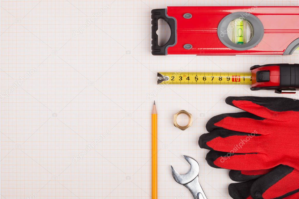Protective gloves, measuring instruments and wrench on top of graph paper.