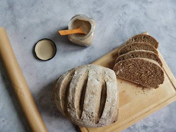 Çavdar ekmeği ekmeği ekmek kağıdının ve cam kavanozun yanında duruyor. 