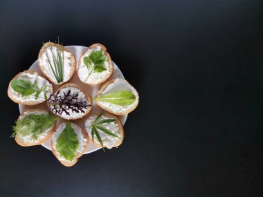 Farklı yeşillikli sandviçler, beyaz tabakta peynir ve koyu bir arka plan. 