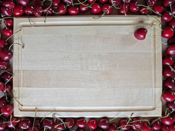 Fundo retangular de madeira em torno do qual se encontra cerejas maduras — Fotografia de Stock