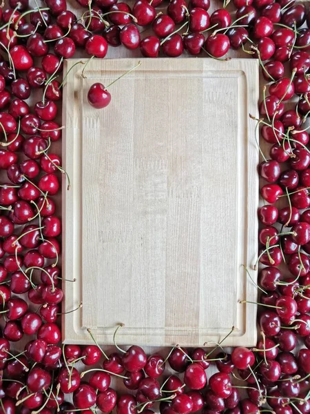wooden rectangular background around which lies ripe cherries