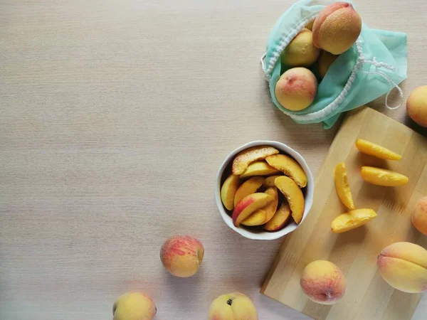 juicy sliced peaches in a plate, next to whole peaches in a reusable bag, photo with copy space