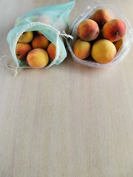 Şeftaliler plastik poşette ve yeniden kullanılabilir poşette. Kopyalama alanı olan dikey fotoğraf