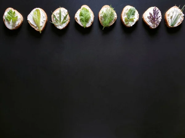 Koyu bir arka planda farklı yeşillikte ve peynirli sandviçler. 