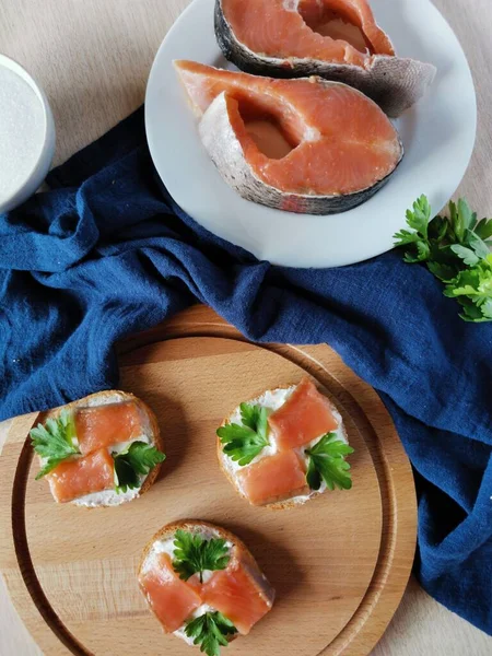 Slices of red fish homemade salt on a white plate and sandwiches with her decorated with blue textiles — Stock Photo, Image