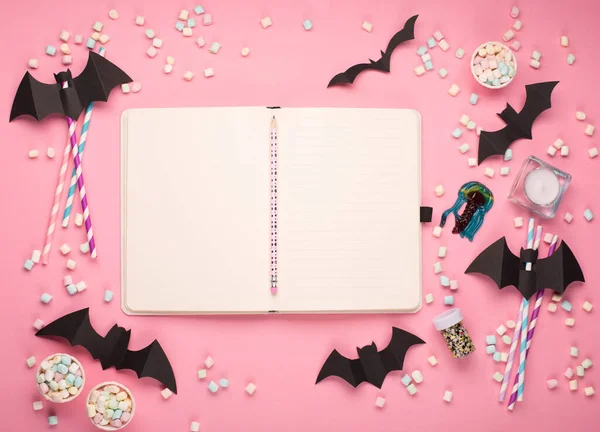 Happy Halloween holiday concept. Halloween decorations, black bats, candy on paper pink background. Halloween party greeting card mockup with copy space. Flat lay, top view, overhead.