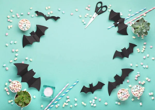 Happy Halloween holiday concept. Halloween decorations, black bats, candy on paper green mint background. Halloween party greeting card mockup with copy space. Flat lay, top view, overhead.