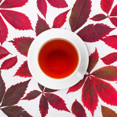 Sonbahar yaratıcı kompozisyonu. Kırmızı yapraklar, yabani üzümler, beyaz ahşap arka planda bir fincan çay. Sonbahar, Şükran Günü konsepti. Düz konum, üst görünüm, kopyalama alanı.