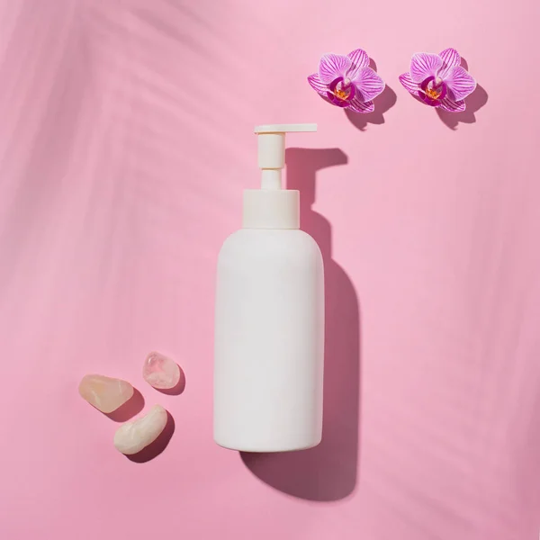 Minimal background for branding and product presentation. White cosmetic bottle with pink flower phalaenopsis orchid and shadow palm leaves. Beauty SPA branding mock-up.