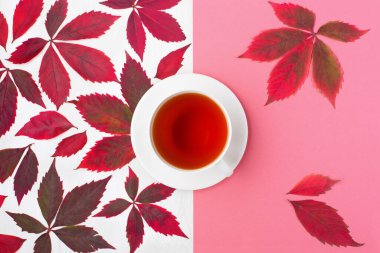 Sonbahar yaratıcı kompozisyonu. Kırmızı yapraklar, yabani üzümler, beyaz ahşap arka planda bir fincan çay. Sonbahar, Şükran Günü konsepti. Düz konum, üst görünüm, kopyalama alanı.