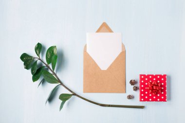 Noel 'in boş beyaz kartı, el işi zarfı ve küçük kırmızı hediyeli ahşap bir arka plan. Düz konum, üst görünüm, kopyalama alanı. Asgari tasarım modeli.