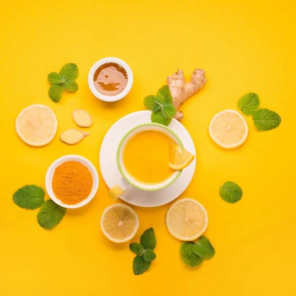 Herbal tea of turmeric with mint, ginger, lemon, honey on paper yellow background. Spicy medicinal tea for autumn or winter season. Flat lay, top view. Healthy food and drink concept.