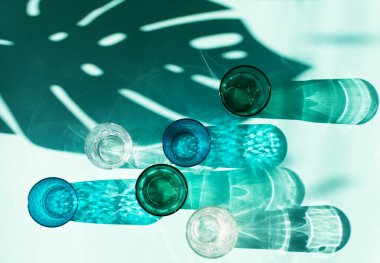 Mavi nane arkaplanındaki boş bardaklar. Gözlükler ve gölgeler arasında sert bir ışık. Temiz minimalist çağdaş sanat. Basit görsel konsept. AI Aqua 2021 yılının moda rengi. Düz yatıyordu. Üst görünüm.