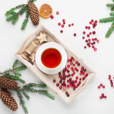 Sıfır Noel konsepti. Doğal Noel süsü, bir fincan çay, taze kızılcık, kozalak ve beyaz ahşap arka planda dallar. Düz yerde, üst tarafta. Tatil metni için boş alan.
