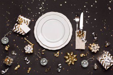 Beyaz tabak, çatal bıçak takımı ve siyah arka planda gümüş Noel süslemeleri olan Noel ya da yeni yıl sofrası. Üst görünüm, kopyalama alanı, düz uzanma