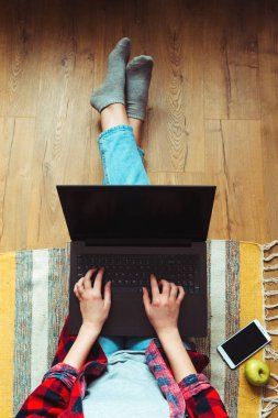 Kız kot pantolon ile bir dizüstü bilgisayar. Çalışma süreci. Katta oturuyor. Telefon ve elma.