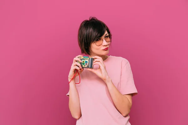 Joven chica bonita en gafas de sol con cámara hipster. Fondo de color. Rosa — Foto de Stock
