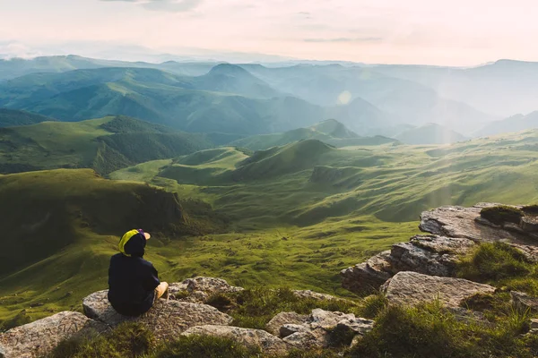 Travel man tourist sitting alone on the edge mountains over green valley adventure lifestyle extreme vacations green landscape Freedom — Stock Photo, Image