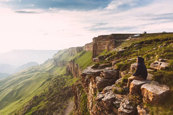 Travel man tourist alone on the edge caucasus rock mountains adventure lifestyle extreme vacations green sunset landscape — Stock Photo, Image