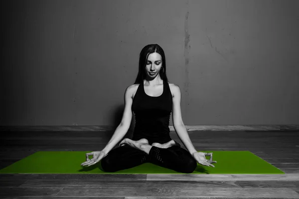 Schwarz-Weiß-Foto von jungen schönen Frau Brünette in schwarzer Kleidung Praxis Yoga Padmasana in dunklem Studio grüne Matte Sport Meditation monochrom — Stockfoto