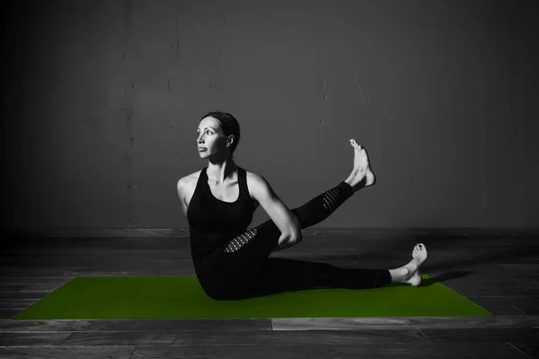 Black white photo of Young beautiful woman brunette in black clothes practice yoga marichyasana in dark studio green mat Sport meditation monochrome — Stock Photo, Image