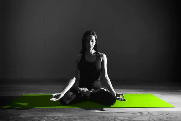 Black white photo of Young beautiful woman brunette in black clothes practice yoga Padmasana in dark studio green mat Sport meditation monochrome — Stock Photo, Image