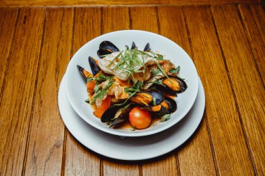 Tahta bir masada sebzeli kızarmış deniz ürünleri. Kabuklu midyeler, kalamar, domates, kırmızı biber.