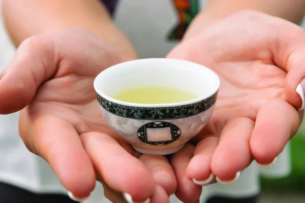 A small cup with yellow tea in the hands. Close-up. Asian tea