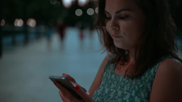 美しい女性ピンクの爪で青いドレスで公園で夕暮れ時のチャットやスマートフォン上のテキスト ウェブスクロールスローモーション — ストック動画