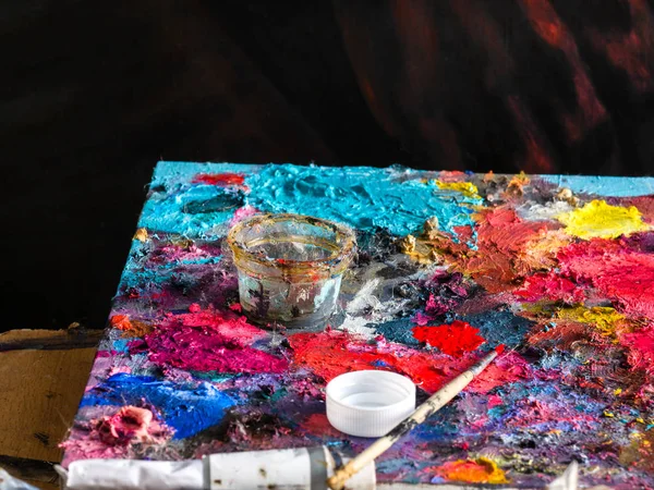 在杯子和油色管的画家用画笔与亚麻籽油的颜色在调色板上特写彩色和纹理 — 图库照片