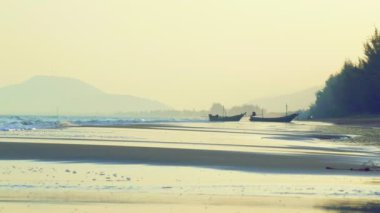 Akşamları dalgalar ve sörfler Tayland 'da arka planda balıkçı teknesiyle sahile çarpıyor..