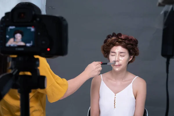 The makeup artist was doing the makeup for the model while the video was being recorded.