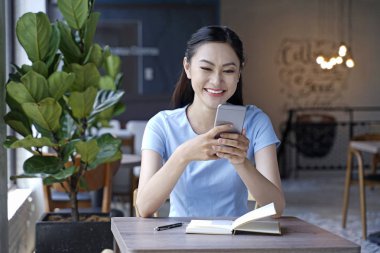 Asyalı oldukça çekici kadın akıllı kullanarak kahve dükkanında oturan