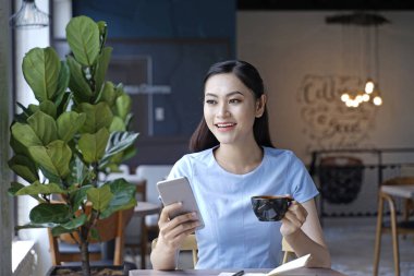 Asyalı oldukça çekici kadın akıllı kullanarak kahve dükkanında oturan