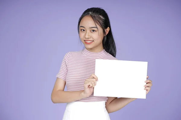 ピンクのシャツで空白のメッセージホワイトボードを持つアジアの若い十代の美しい陽気な女の子, 紫の背景に — ストック写真