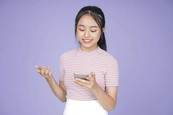 Asiática joven adolescente hermosa chica alegre con teléfono inteligente en camisa rosa, sobre fondo violeta — Foto de Stock