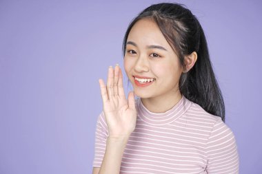 El hareketi fısıltı pembe gömlek ile Asyalı genç genç güzel neşeli kız, mor arka plan