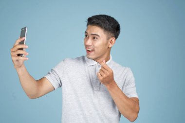 Akıllı telefon ile Asyalı genç yakışıklı çekici adam mavi arka plan üzerinde selfie fotoğraf çekmek