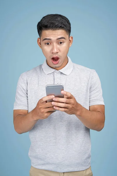 Asian młody przystojny atrakcyjny człowiek z inteligentny telefon na niebieski tło — Zdjęcie stockowe