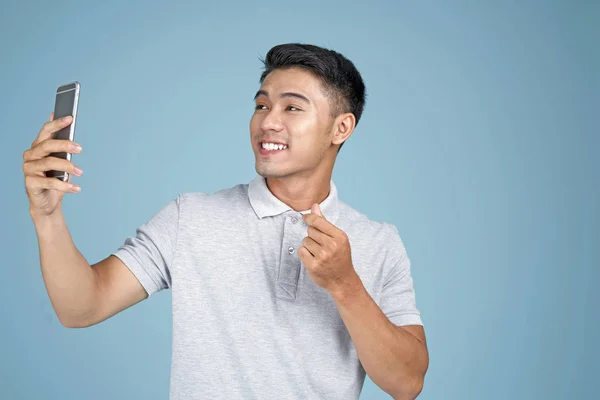 Asiatische junge hübsche attraktive Mann mit Smartphone machen ein Selfie Foto auf blauem Hintergrund — Stockfoto
