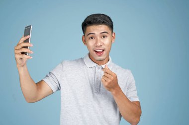 Akıllı telefon ile Asyalı genç yakışıklı çekici adam mavi arka plan üzerinde selfie fotoğraf çekmek