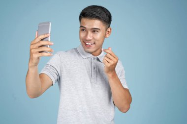 Akıllı telefon ile Asyalı genç yakışıklı çekici adam mavi arka plan üzerinde selfie fotoğraf çekmek