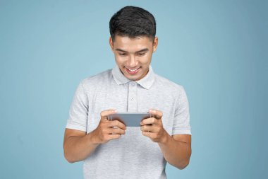Mavi arka plan üzerinde akıllı telefon ile oyun oynayan Asyalı genç yakışıklı çekici adam