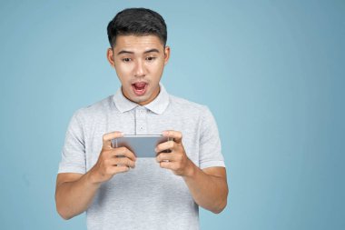 Mavi arka plan üzerinde akıllı telefon ile oyun oynayan Asyalı genç yakışıklı çekici adam