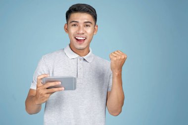 Mavi arka plan üzerinde akıllı telefon ile oyun oynayan Asyalı genç yakışıklı çekici adam